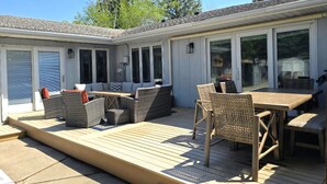 Een overdekt terras met buitenmeubilair, een terras en een gebouw met grote ramen en deuren.