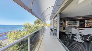 Un balcon avec vue sur la mer, un coin bar avec des tabourets et un espace salon avec des tables.