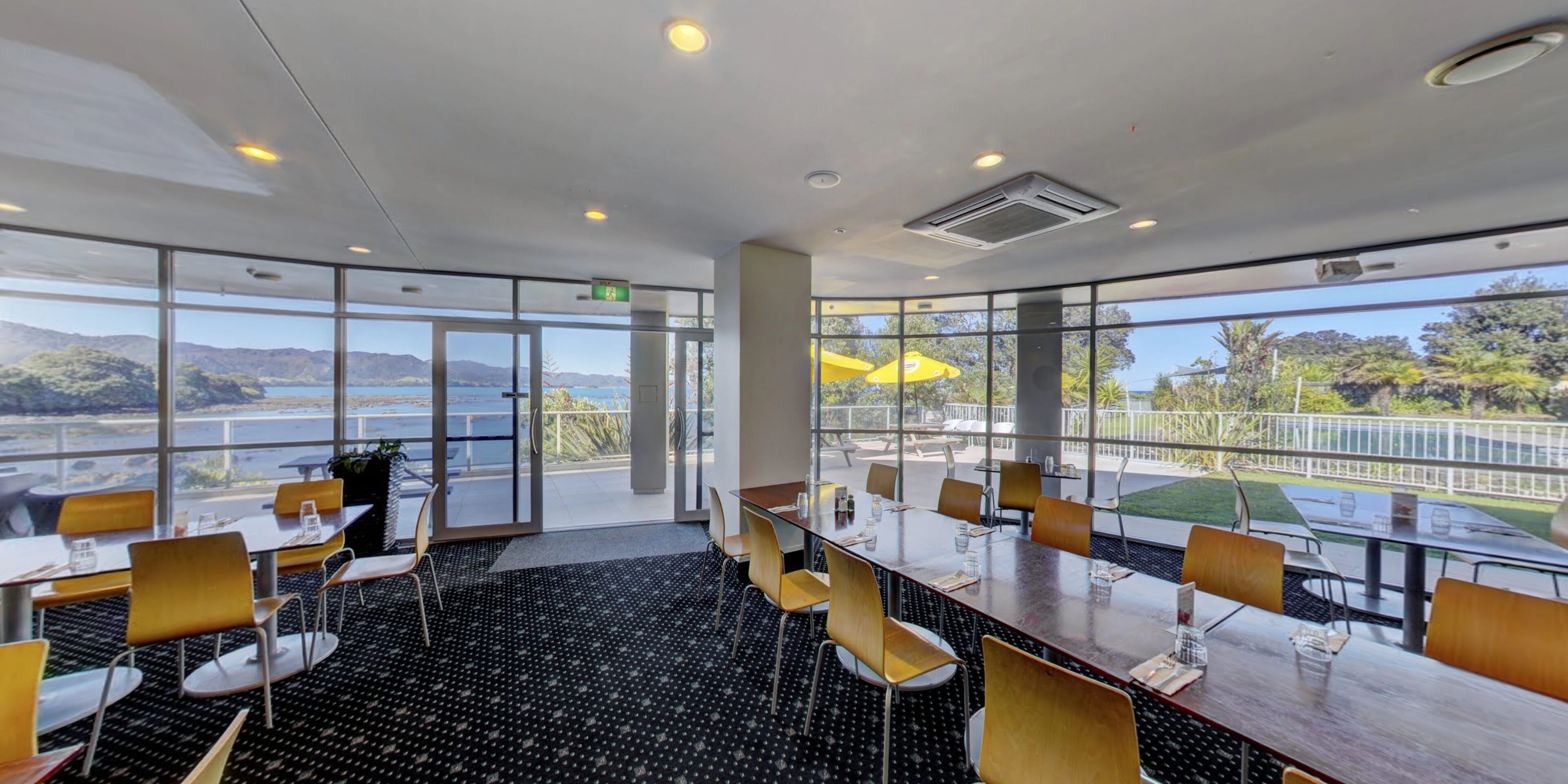 Un salón de conferencias con ventanas amplias, vista a un lago y mobiliario exterior.
