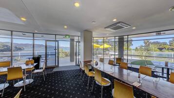 Un salón de conferencias con ventanas amplias, vista a un lago y mobiliario exterior.
