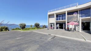 Un bâtiment moderne offrant une vue sur la plage, avec un restaurant et un espace extérieur aménagé pour les clients.