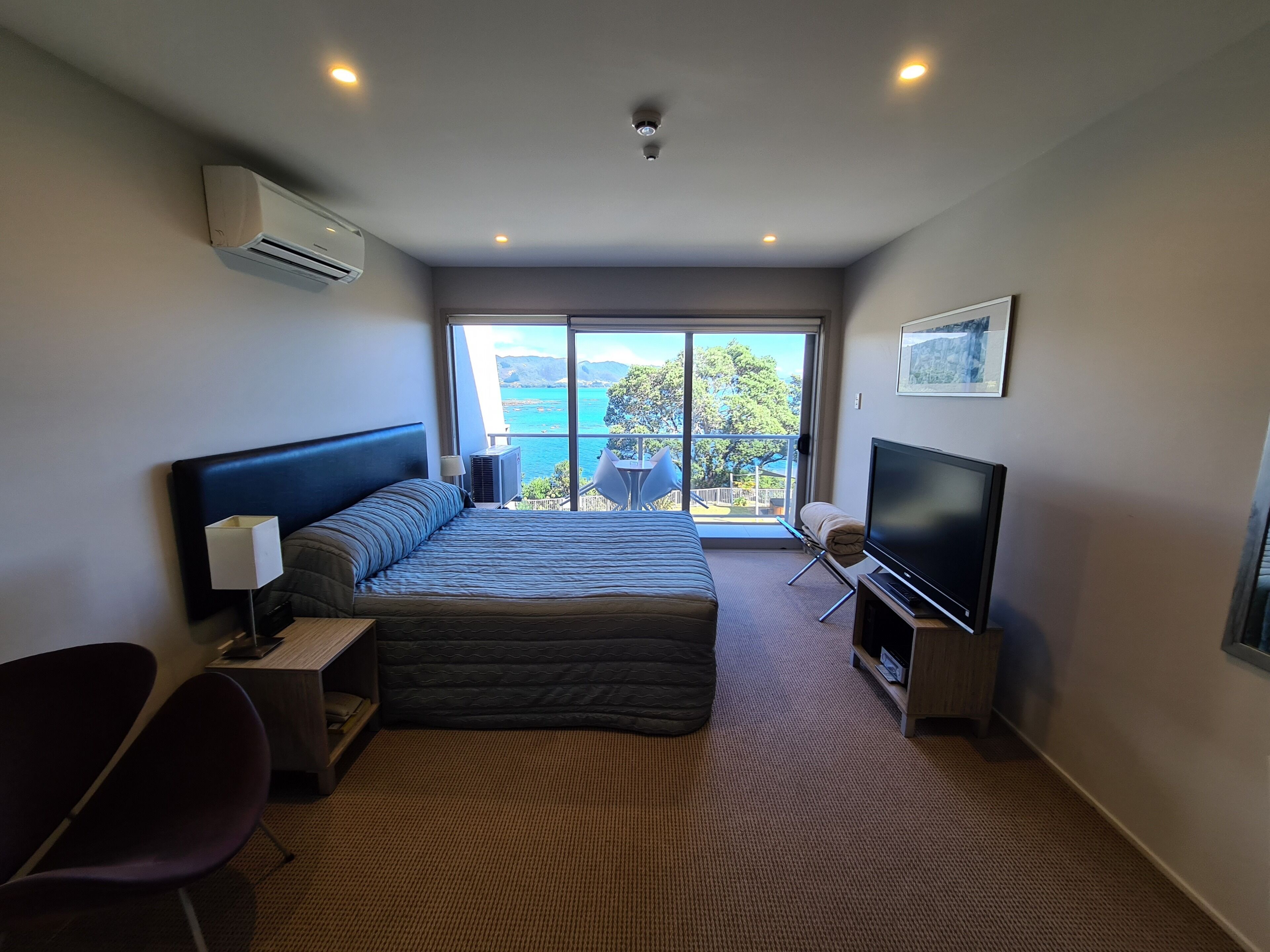 A modern hotel room with a large bed, a flat-screen TV, a desk, and a chair.