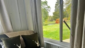 Huoneessa on sohva, pieni puinen sivupöytä ja ikkunasta avautuu näkymä puutarhaan.
