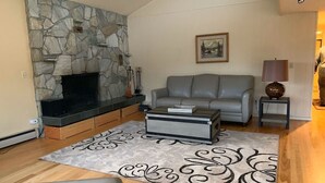 A living room with a stone fireplace, grey sofa, coffee table, and a patterned rug. - Gorgeous home w/Sauna downtown Anchorage. Walk to dine, coffee & attractions (Anchorage)