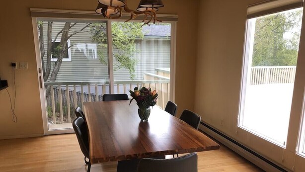 A dining area with a wooden table, six chairs, and a vase with flowers. - Gorgeous home w/Sauna downtown Anchorage. Walk to dine, coffee & attractions (Anchorage)