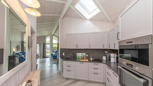 A modern kitchen with white cabinetry, a skylight, and a wooden dining table. - Baltic View - Komfortables, Sehr Strandnahes Ferienhaus mit Whirlpool und Sauna (Brodersby)