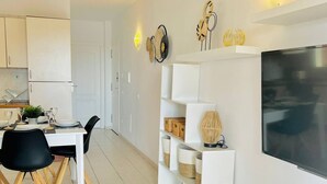 A modern kitchen with white cabinets, a dining table with black chairs, and a TV mounted on the wall. - Ground-Floor 1 bedroom condoPool &Wifi Costa Adeje (Callao Salvaje)