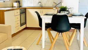 A modern kitchen with white cabinets, a dining table with chairs, and a small round table with a remote control. - Ground-Floor 1 bedroom condoPool &Wifi Costa Adeje (Callao Salvaje)