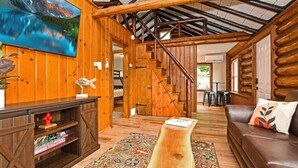 A log cabin interior with a wooden staircase, a sofa, a coffee table, and a painting on the wall. - Walk to Beach - Close to Town - Pet Friendly Cabin (Lake George)