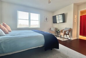 Quarto com cama, televisão na parede, cadeira e janela com persianas.