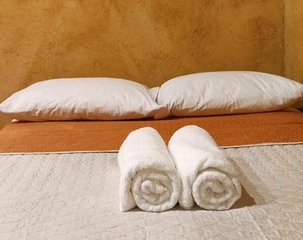 A bed with white pillows and two rolled white towels on a white quilted mattress. - Ixak Cabañas  (Huehuetlán)