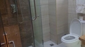 Un baño con ducha acristalada, inodoro y toalla colgada en un perchero.
