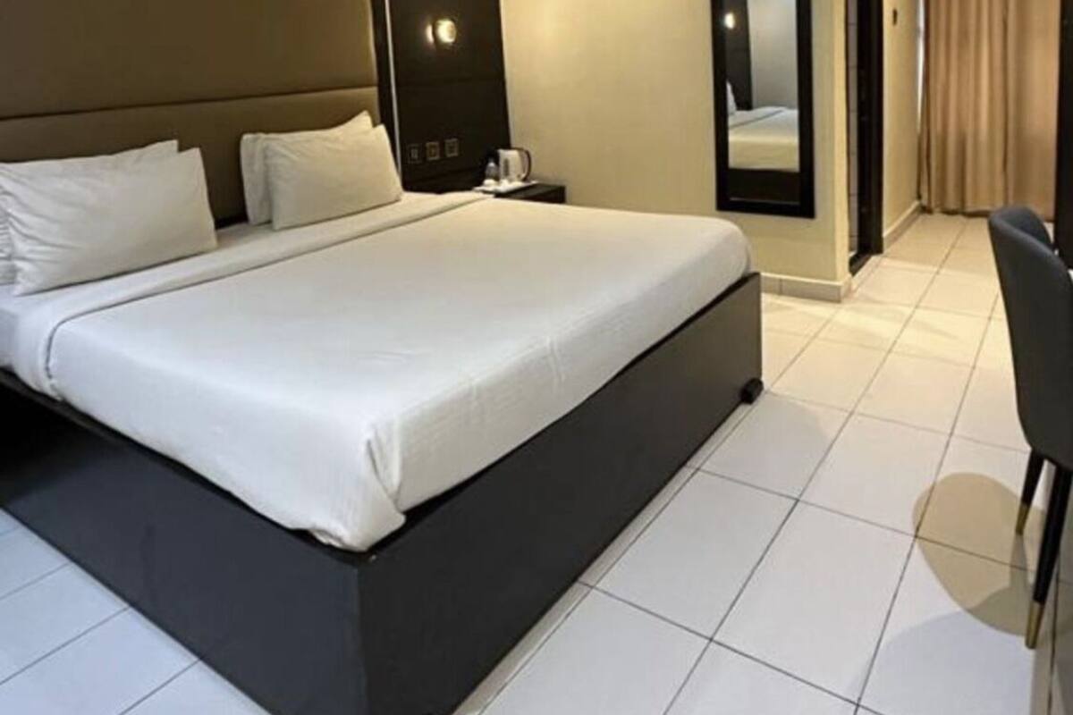A modern hotel room with a large bed, a bedside table, a mirror, and a chair.