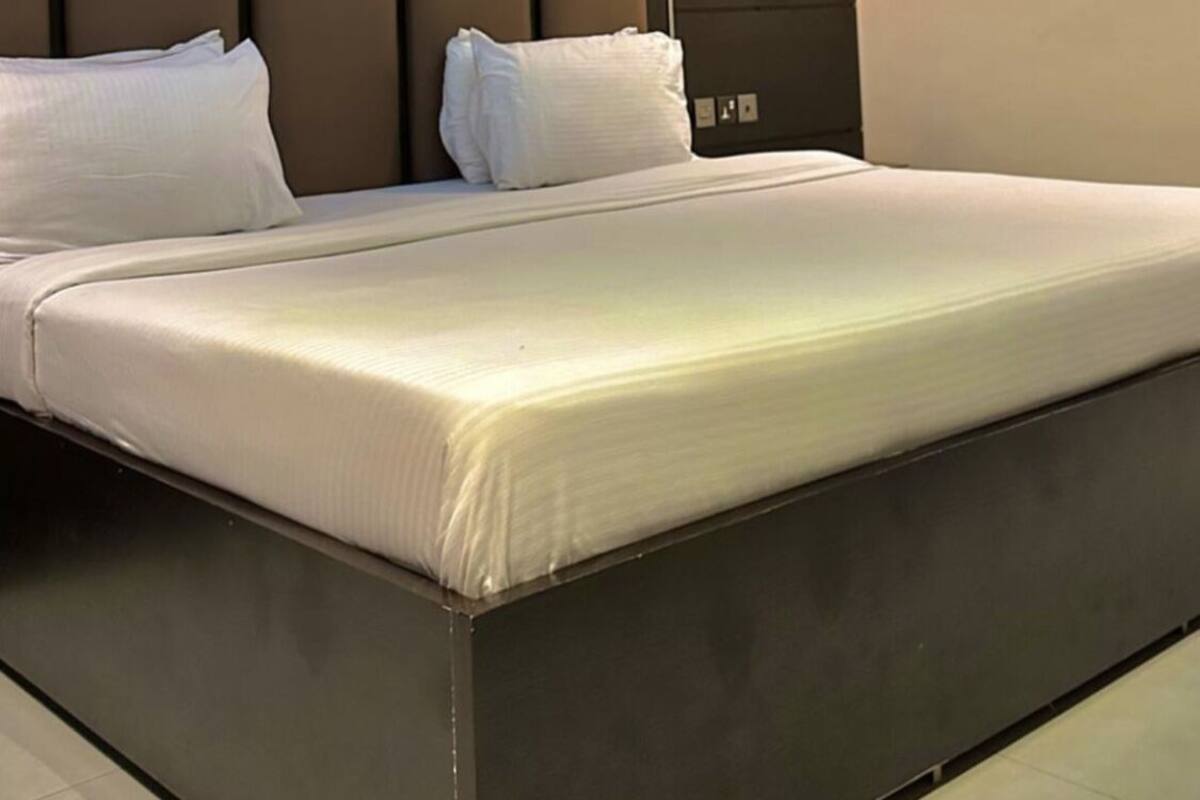A modern hotel room with a large bed, a headboard with vertical panels, and a wall-mounted light.