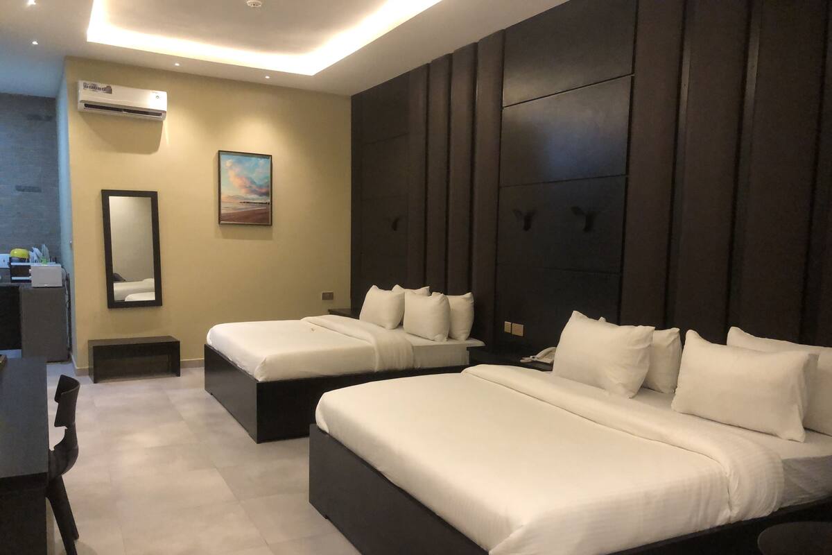 A modern hotel room with two beds, a large mirror, an air conditioning unit, and a painting on the wall.