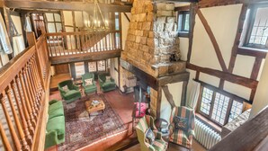 A high-ceiling room with exposed wooden beams, a stone fireplace, and a view of the outdoors through large windows. - 6 bedroom accommodation in East Grinstead (East Grinstead)