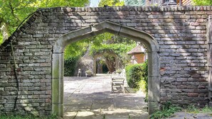A stone archway leading to a paved courtyard with a bench and a statue. - 6 bedroom accommodation in East Grinstead (East Grinstead)