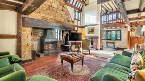 A spacious living room with exposed wooden beams, a stone fireplace, and a large window. - 6 bedroom accommodation in East Grinstead (East Grinstead)