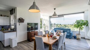 Une cuisine moderne équipée d’un téléviseur, d’une table à manger et de chaises, ainsi que d’un balcon avec un canapé et une vue sur la campagne.