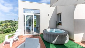 Une terrasse extérieure moderne, dotée d’une porte vitrée donnant sur un balcon, d’un coin salon circulaire en osier et d’une petite fenêtre agrémentée d’une plante.