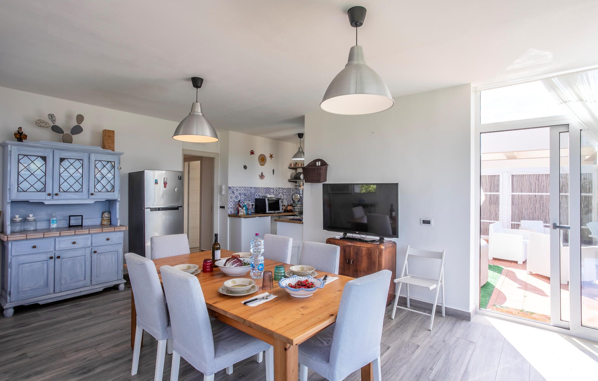 Eine moderne Küche mit einem Holzespeisetisch, weißen Stühlen, einem eingebauten Kühlschrank und einem Fernseher.