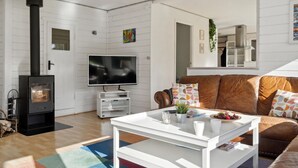 Uma sala de estar com lareira, TV, sofá de couro marrom e mesa de centro branca.