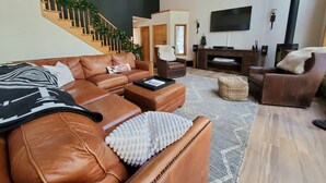 A modern living room with a brown leather sofa, a coffee table, and a fireplace. A staircase with a garland is visible in the background.