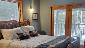 A wooden bed with white bedding, a wooden headboard, and a view of trees through a window.