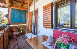 Een houten chalet met een veranda, een schommel en een tafel met een stenen decoratiestuk.