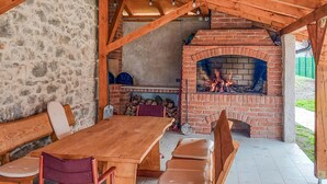 Un área de comedor exterior de madera con chimenea de ladrillo, paredes de piedra y piso de baldosas.