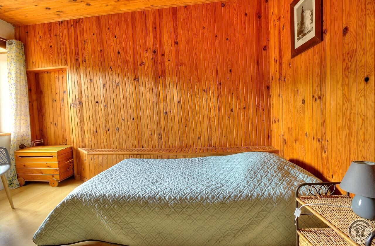 A wooden-paneled bedroom with a bed, a nightstand, a lamp, and a picture on the wall.