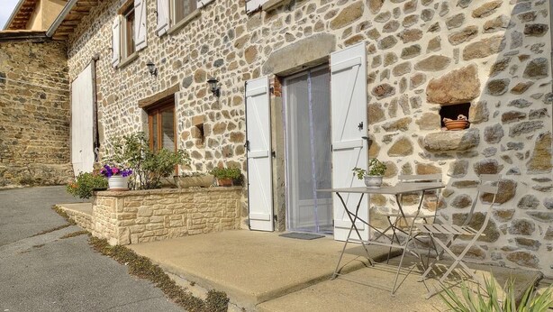 Un bâtiment en pierre doté d’un petit porche, d’une table et de plantes en pot.