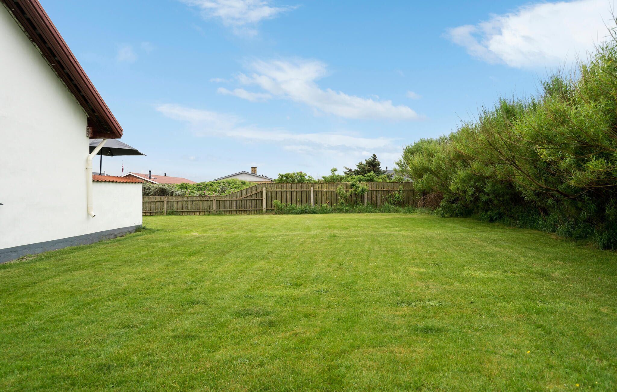 Un jardin avec une clôture en bois, un bâtiment blanc et une pelouse verdoyante.
