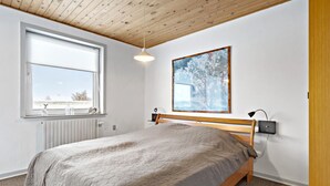 A bedroom with a wooden bed, a window with blinds, a radiator, a wall-mounted lamp, and a framed picture. - 3 bedroom pet friendly home in Ulfborg (Ulfborg)