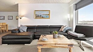 A modern living room with a black leather sofa, a wooden coffee table, and a painting of a coastal scene. - 3 bedroom pet friendly home in Ulfborg (Ulfborg)