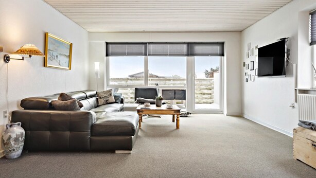 A modern living room with a sectional sofa, a coffee table, and a TV mounted on the wall. - 3 bedroom pet friendly home in Ulfborg (Ulfborg)