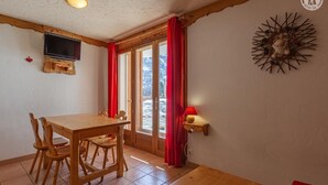 Un tavolo da pranzo in legno con sedie, una televisione fissata al muro, una tenda rossa e una lampada a parete.