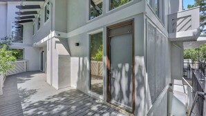 Een modern meerlaags gebouw met een houten terras, grote schuifdeuren en een witte gevel.