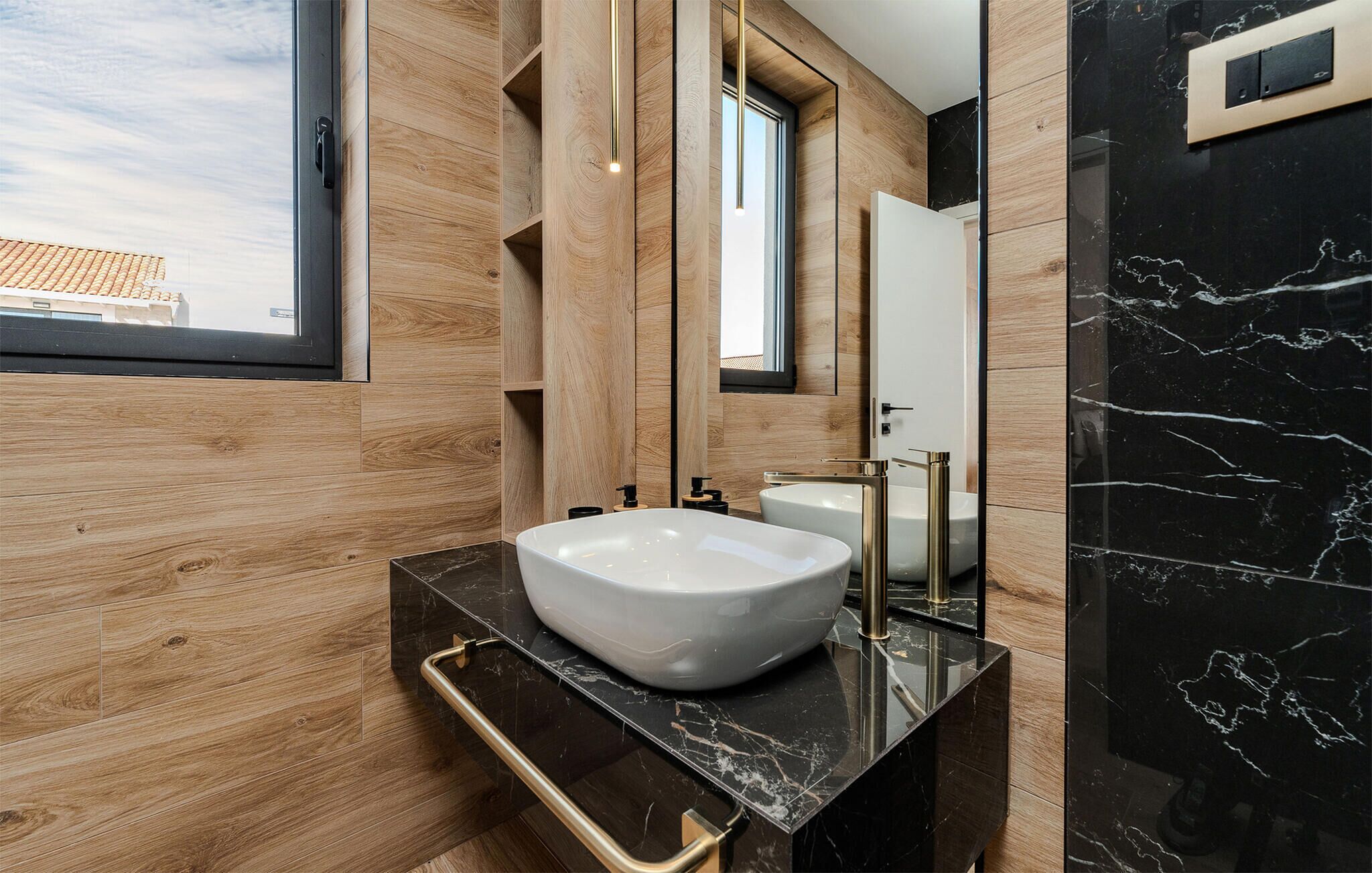 A modern bathroom with a large wooden vanity, a white vessel sink, and a black marble wall.