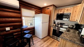 A compact kitchen with a refrigerator, microwave, oven, and sink. There is a small dining area with a table and two stools. - Walk to Beach - Close to Town - Pet Friendly Cabin (Lake George)