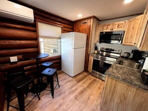 A compact kitchen with a refrigerator, microwave, oven, and sink. There is a small dining area with a table and two stools. - Walk to Beach - Close to Town - Pet Friendly Cabin (Lake George)