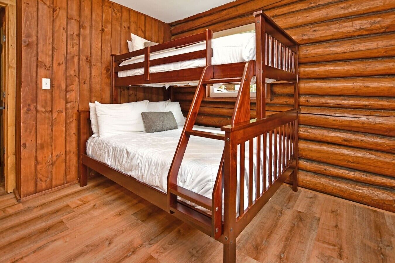 A bunk bed with a wooden frame and white bedding in a room with wooden walls and floors.