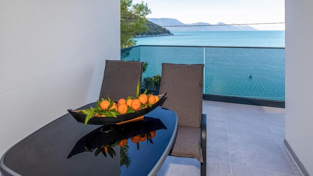 Un balcone con un tavolo che sorregge una ciotola di arance, due sedie e vista sul mare.