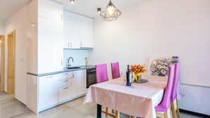 Una cucina moderna con mobili bianchi, forno integrato e lavello. C'è un tavolo da pranzo con sedie rosa e un vaso di fiori.