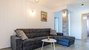 Un soggiorno con un divano grigio, due cuscini decorati, un piccolo tavolino con una bottiglia e un quadro appeso al muro.