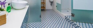 Bathroom features a pedestal sink, toilet, and shower area with a wicker basket and plant.