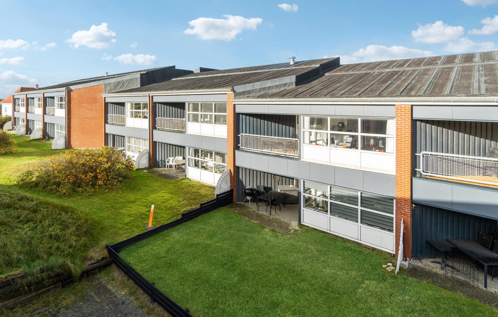 A modern multi-story building with balconies, a grassy courtyard, and a clear sky.