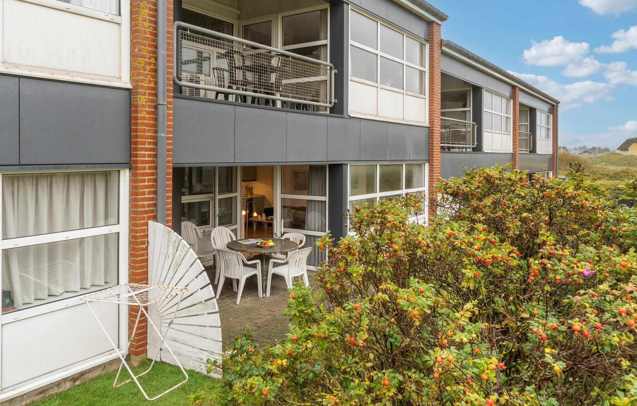 Un bâtiment à deux étages doté d’un balcon, d’un espace repas avec mobilier d’extérieur et d’un jardin avec des arbres fruitiers.