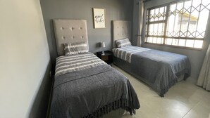 Un dormitorio con dos camas, una mesita de noche con lámpara, una cita enmarcada en la pared y una ventana con vistas.