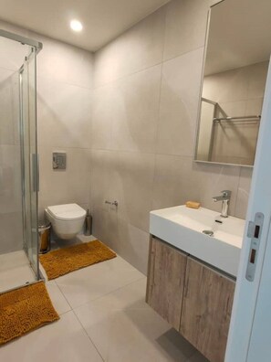 A modern bathroom with a glass shower enclosure, a toilet, a sink with a mirror, and wooden cabinets. - Anchora___ (Paralimni)